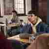 A male student with his hand on his chin sitting at a desk in a high school classroom